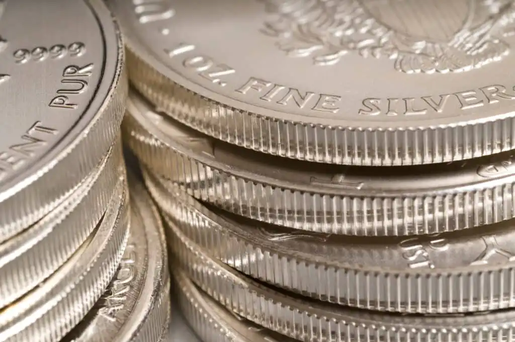 Close-up of neatly stacked silver coins with ridged edges and partial stamped text visible, highlighting their shiny, metallic surfaces.