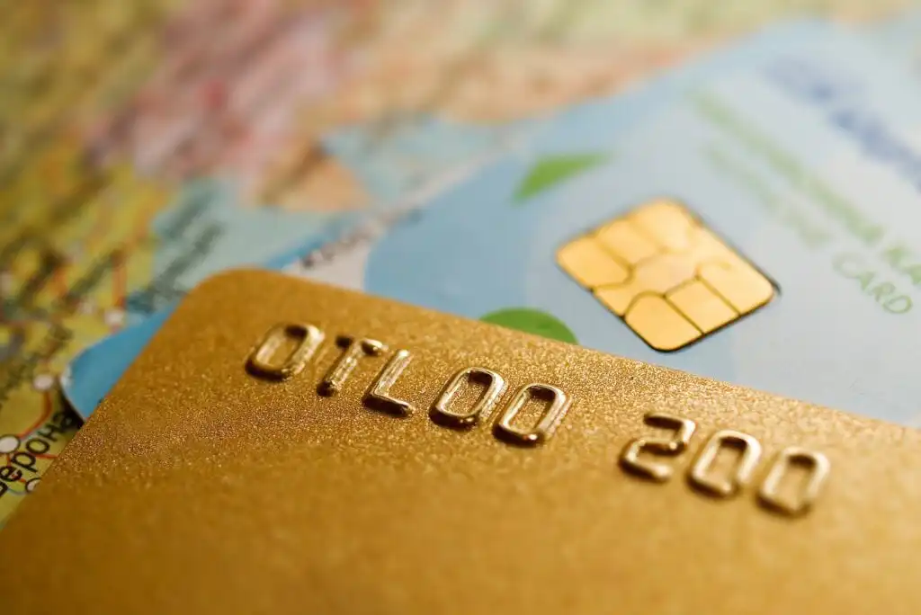 Close-up of two credit cards, one gold and one blue, placed on a map. The gold card’s raised numbers and the blue card’s chip are clearly visible, highlighting travel and payment concepts.