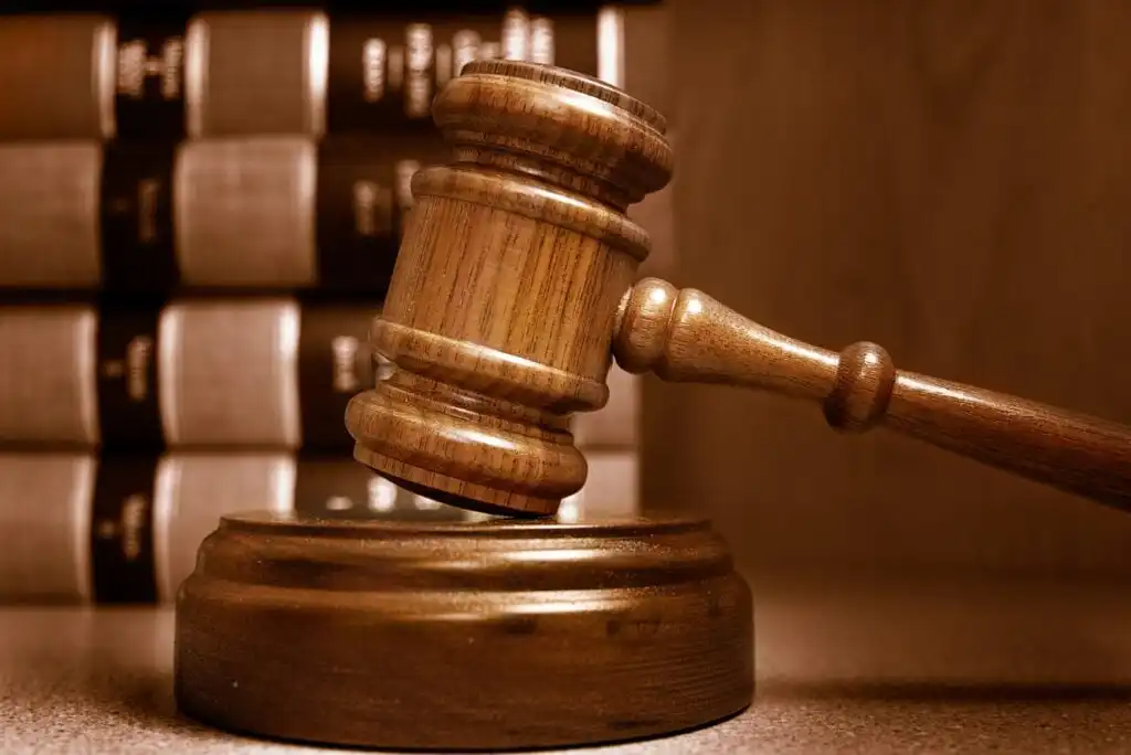 A wooden judges gavel rests on its sound block, with several thick law books stacked in the blurred background, symbolizing justice and legal proceedings.