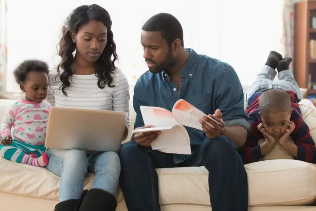 A group of people sitting on a couch looking at a laptop and a child.