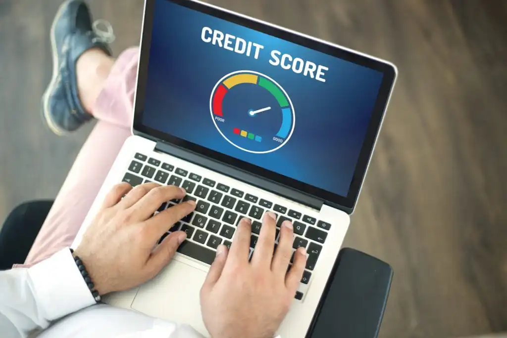 A person typing on a laptop displaying a screen with the words Credit Score and a colorful credit score gauge.