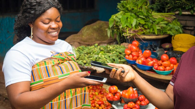 Mulher afro-americana vendendo produtos frescos recebendo pagamento por celular sem contato