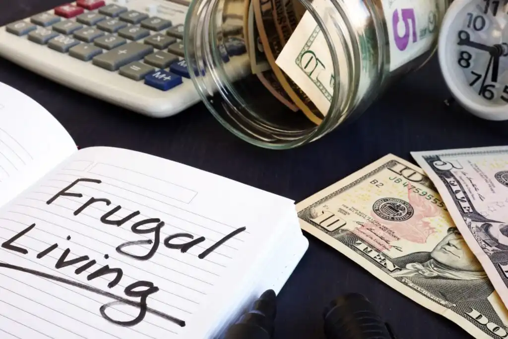 A notebook with “Frugal Living” written on it sits next to a spilled jar of cash, a calculator, and a clock, symbolizing budgeting and saving money.