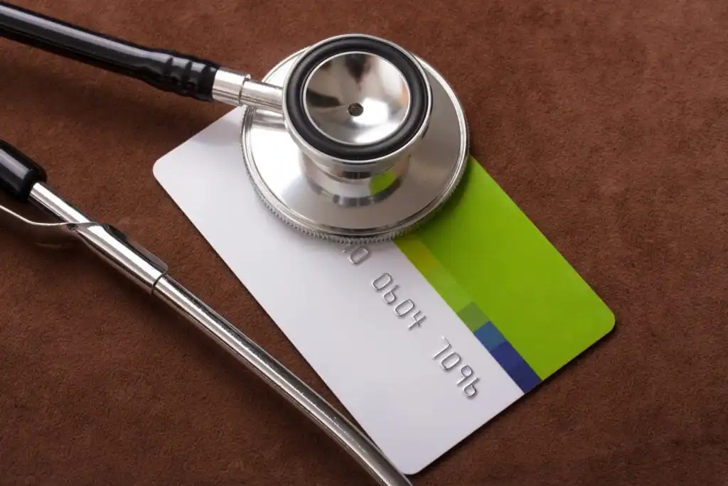 A stethoscope rests on top of a green and white credit or health insurance card, set against a brown background.