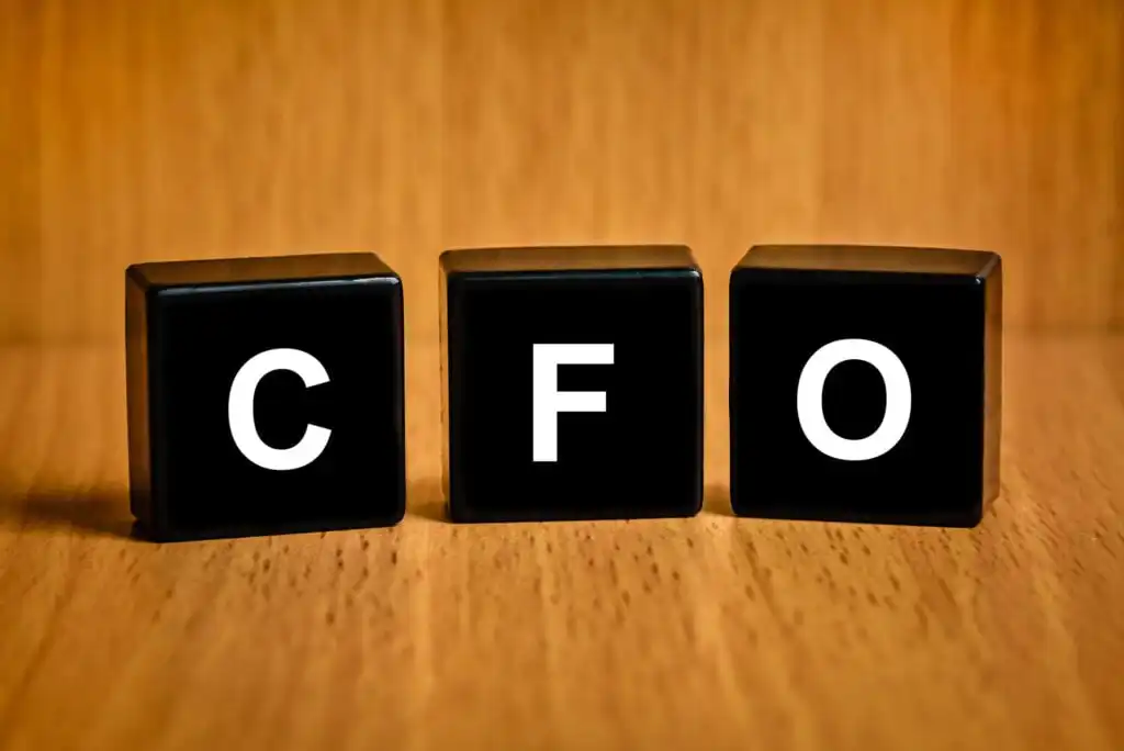 Three black cubes with white letters C, F, and O are arranged side by side on a wooden surface, representing the abbreviation for Chief Financial Officer.