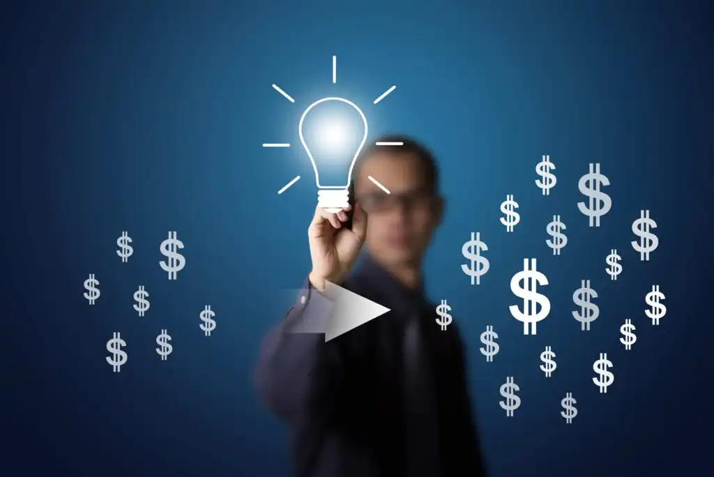 A person in a suit touches a glowing lightbulb icon on a transparent screen, surrounded by floating dollar signs, symbolizing innovative ideas leading to financial success.