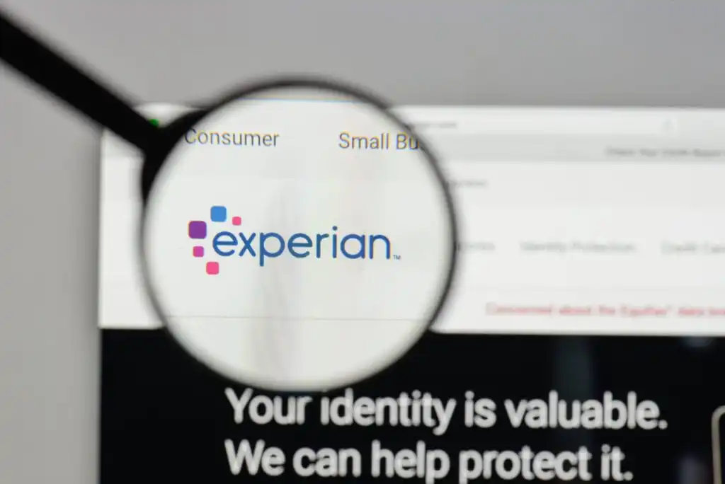 A magnifying glass focuses on the Experian logo displayed on a computer screen, with the words Your identity is valuable. We can help protect it partially visible below.