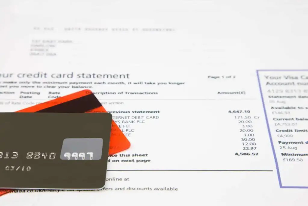 A close-up of two credit cards placed on top of a printed credit card statement, showing various transaction details and account information.