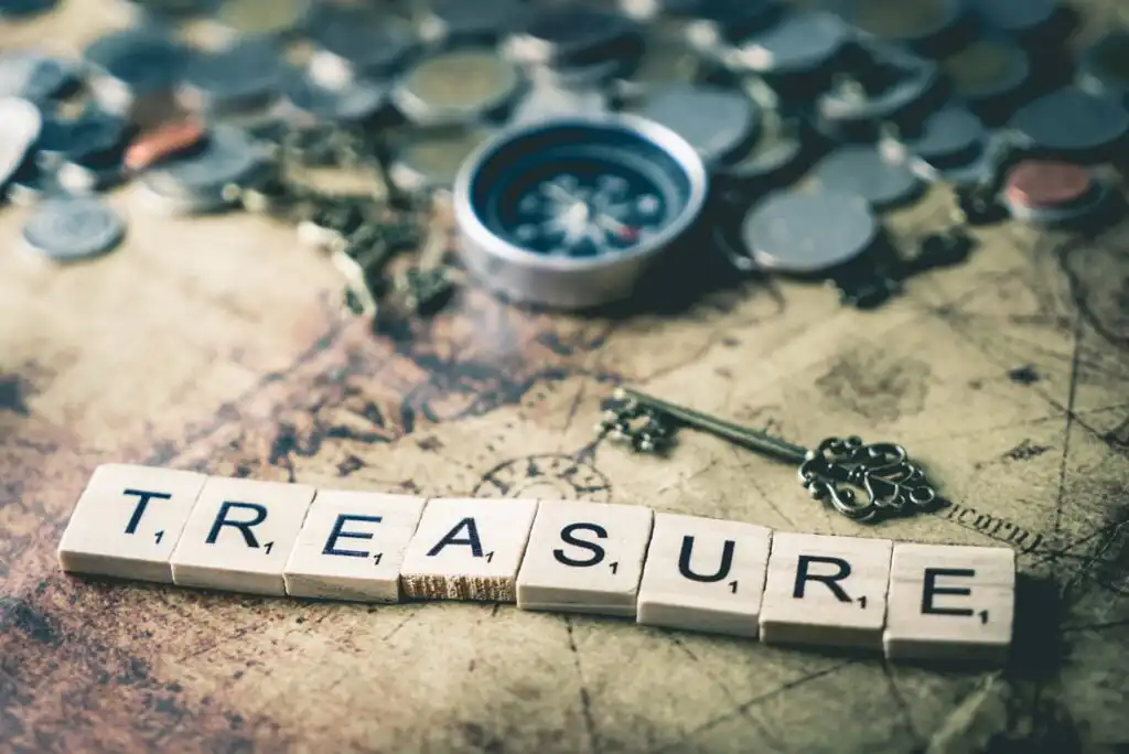 Scrabble tiles spell TREASURE on an old map, with a vintage key, a compass, and scattered coins in the background, evoking a sense of adventure and discovery.
