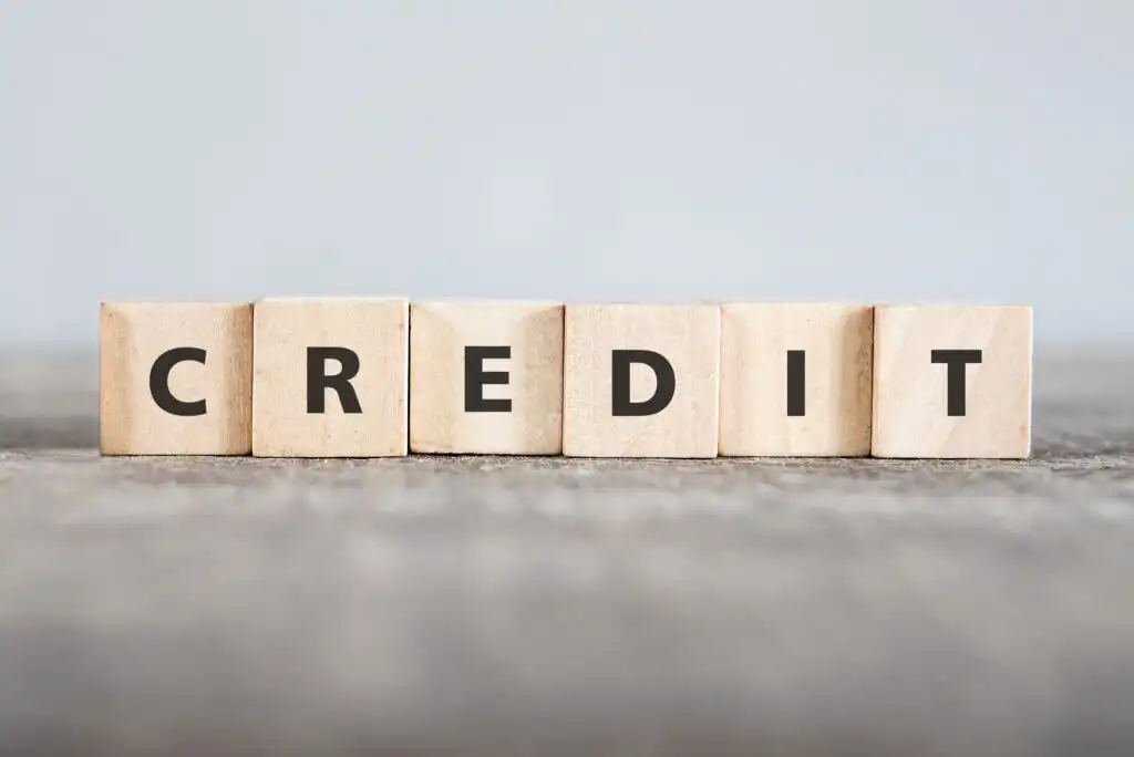 Wooden blocks arranged in a row on a gray surface spell out the word CREDIT in bold black letters, with a blurred light gray background.