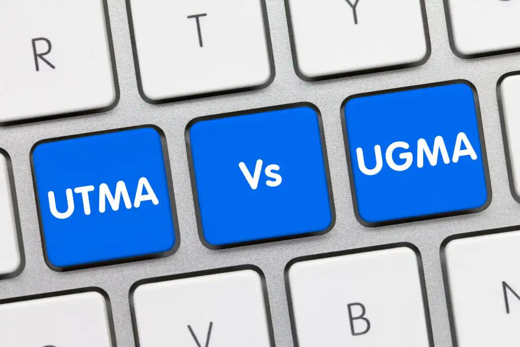 Close-up of a computer keyboard with three blue keys labeled UTMA, Vs, and UGMA, highlighting a comparison between the two financial account types.