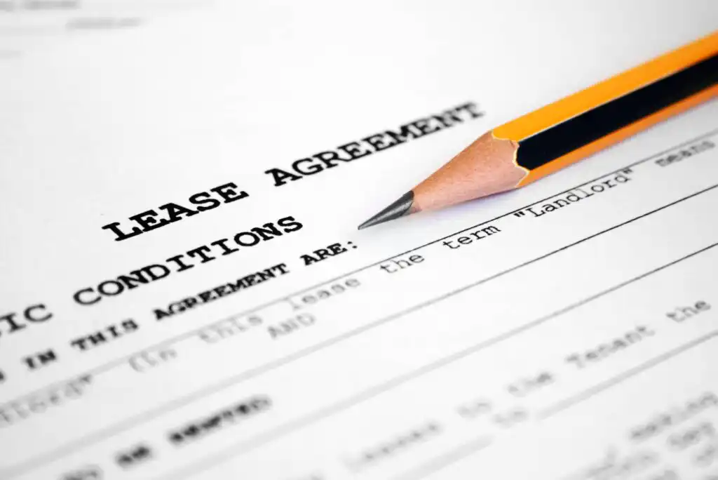 A sharpened yellow pencil rests on a printed lease agreement document, with the words LEASE AGREEMENT and CONDITIONS visible in bold letters on the paper.