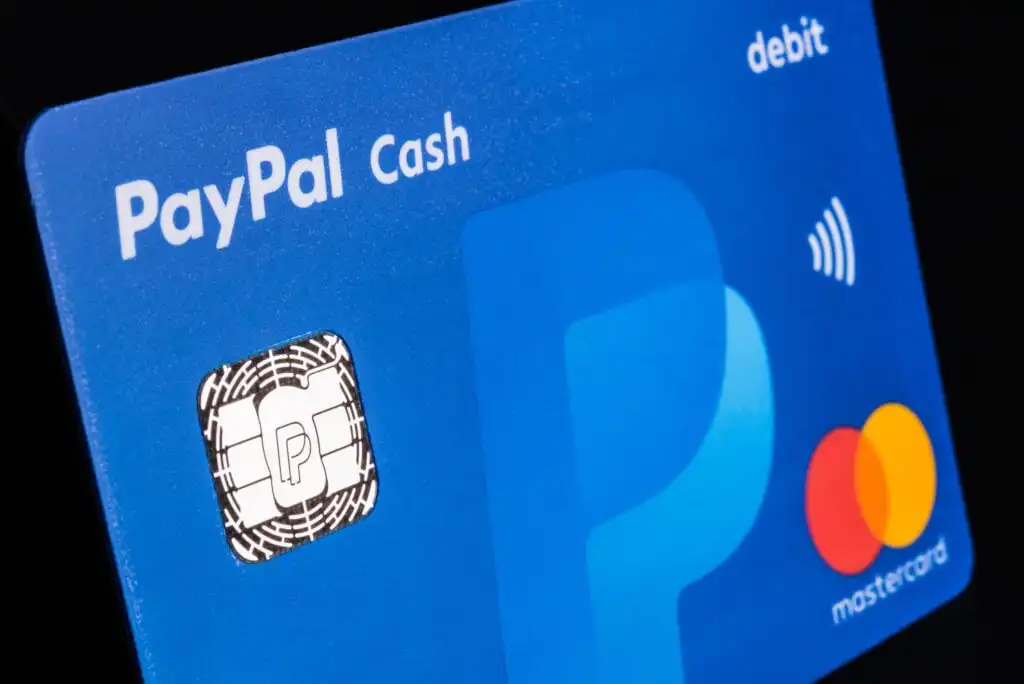 A close-up of a blue PayPal Cash Mastercard debit card, featuring a chip, contactless symbol, large PayPal logo, and Mastercard logo on a black background.