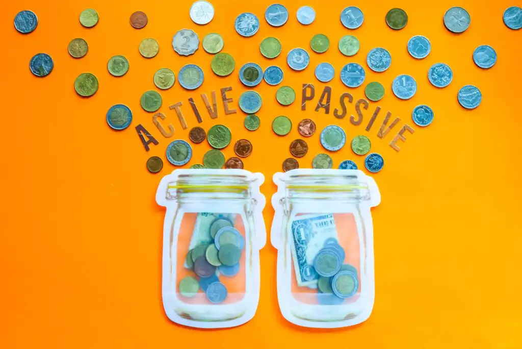 Two jars filled with coins and paper money are labeled “ACTIVE” and “PASSIVE,” with scattered coins above each on an orange background, suggesting different types of income or investment.