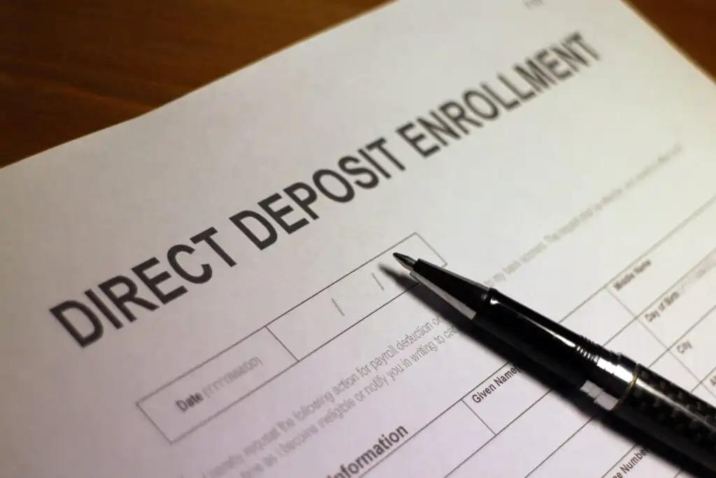 A close-up of a direct deposit enrollment form with a black pen resting on top, ready to be filled out.