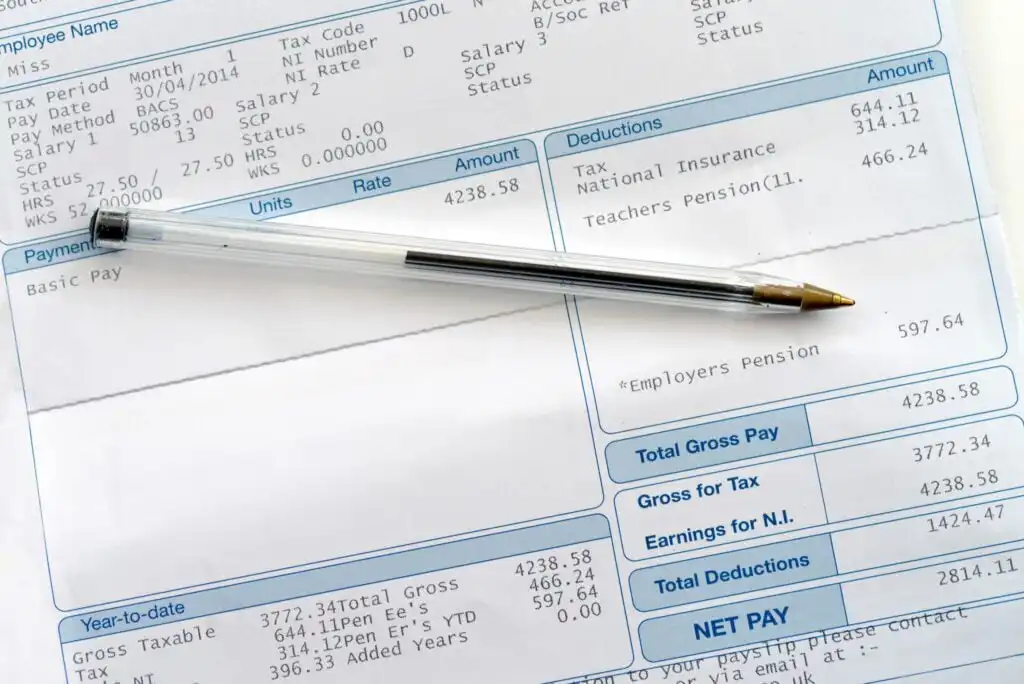 A black ballpoint pen rests on a detailed payslip showing salary, tax, and deductions such as National Insurance and pensions, with figures and payment breakdowns visible.
