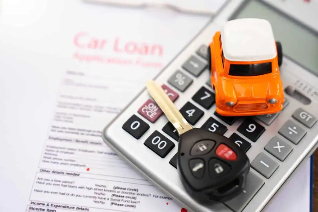A car loan application form with a calculator on top, an orange toy car, and a car key resting on the calculator.