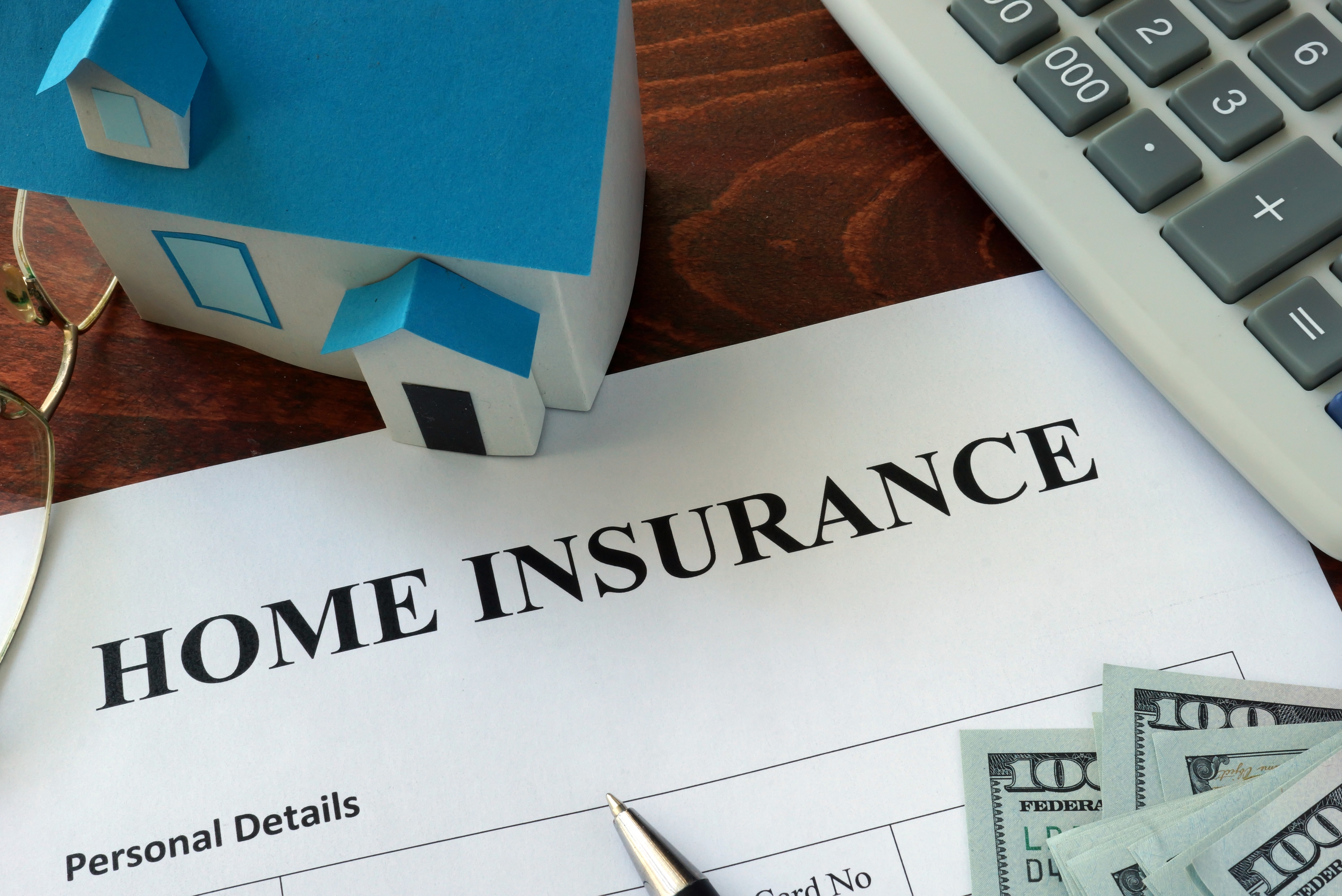 A model-sized home, paper reading "Home insurance," money, and a calculator. 