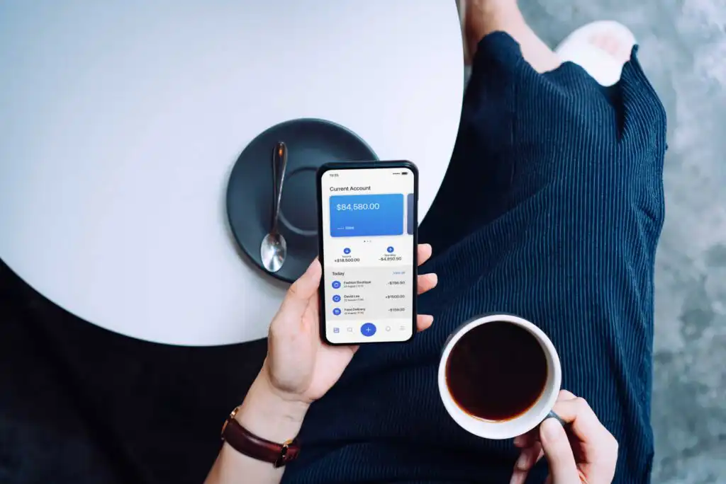 A person holding a phone and a cup of coffee.