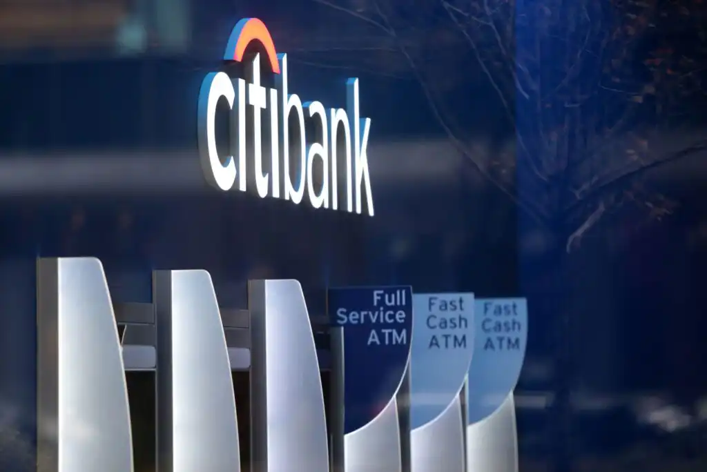 A Citibank sign with the logo above several ATMs, including Full Service and Fast Cash machines, reflected on a glass surface.
