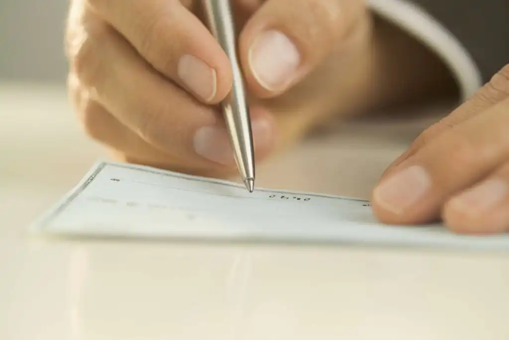 Close-up of a person holding a pen and writing on a blank check placed on a white surface.