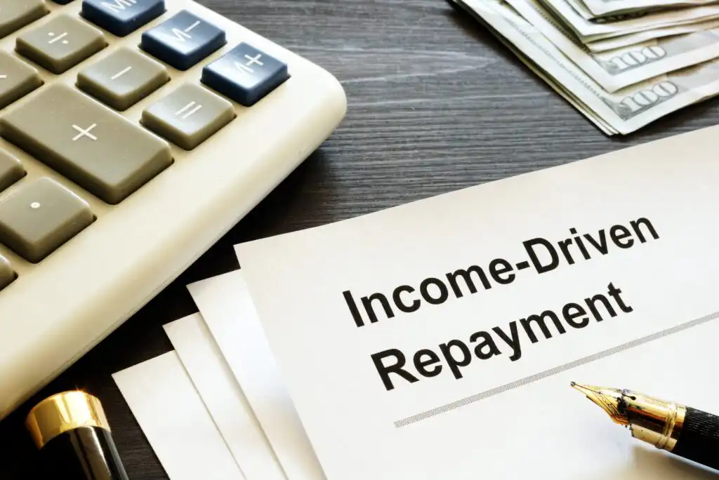 A document labeled Income-Driven Repayment sits on a desk next to a calculator, a stack of cash, and a fountain pen.