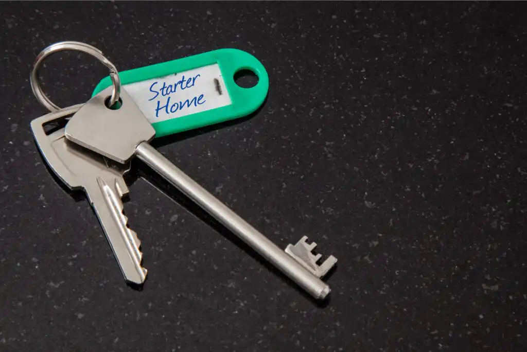 A set of silver keys on a keyring is attached to a green key tag labeled Starter Home, resting on a black, speckled surface.