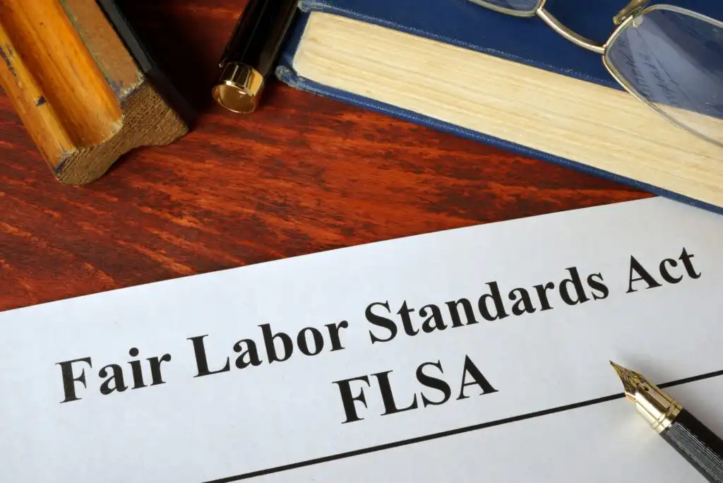A document labeled Fair Labor Standards Act (FLSA) sits on a wooden desk beside a gavel, a pen, and a closed book.