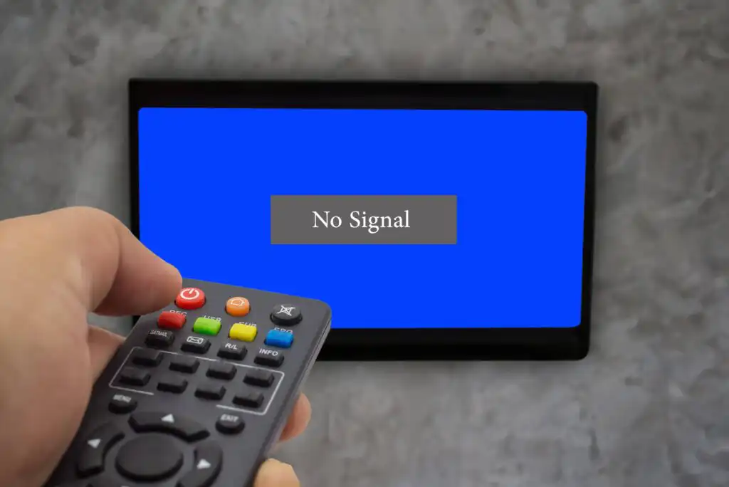 A hand holding a remote control points at a TV screen displaying a solid blue background with a No Signal message in the center.