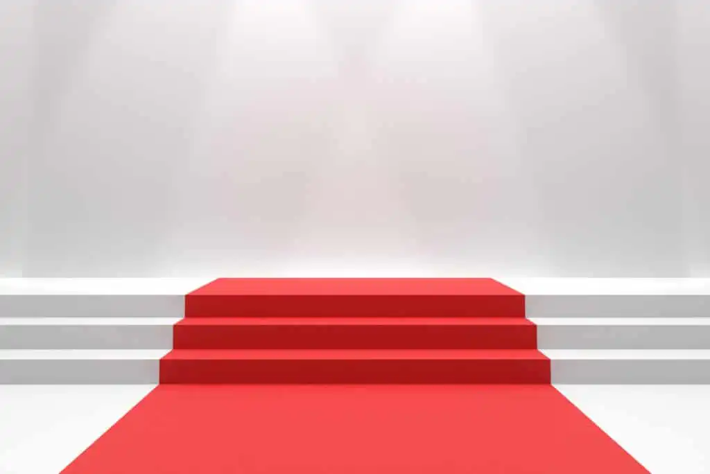 A minimalist scene featuring a red carpet leading up a set of white stairs, with a well-lit, plain white background.
