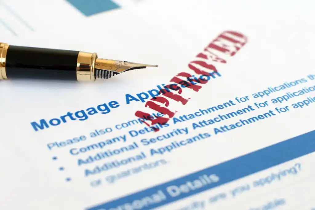 A fountain pen rests on a mortgage application form with the word APPROVED stamped in red across the document.