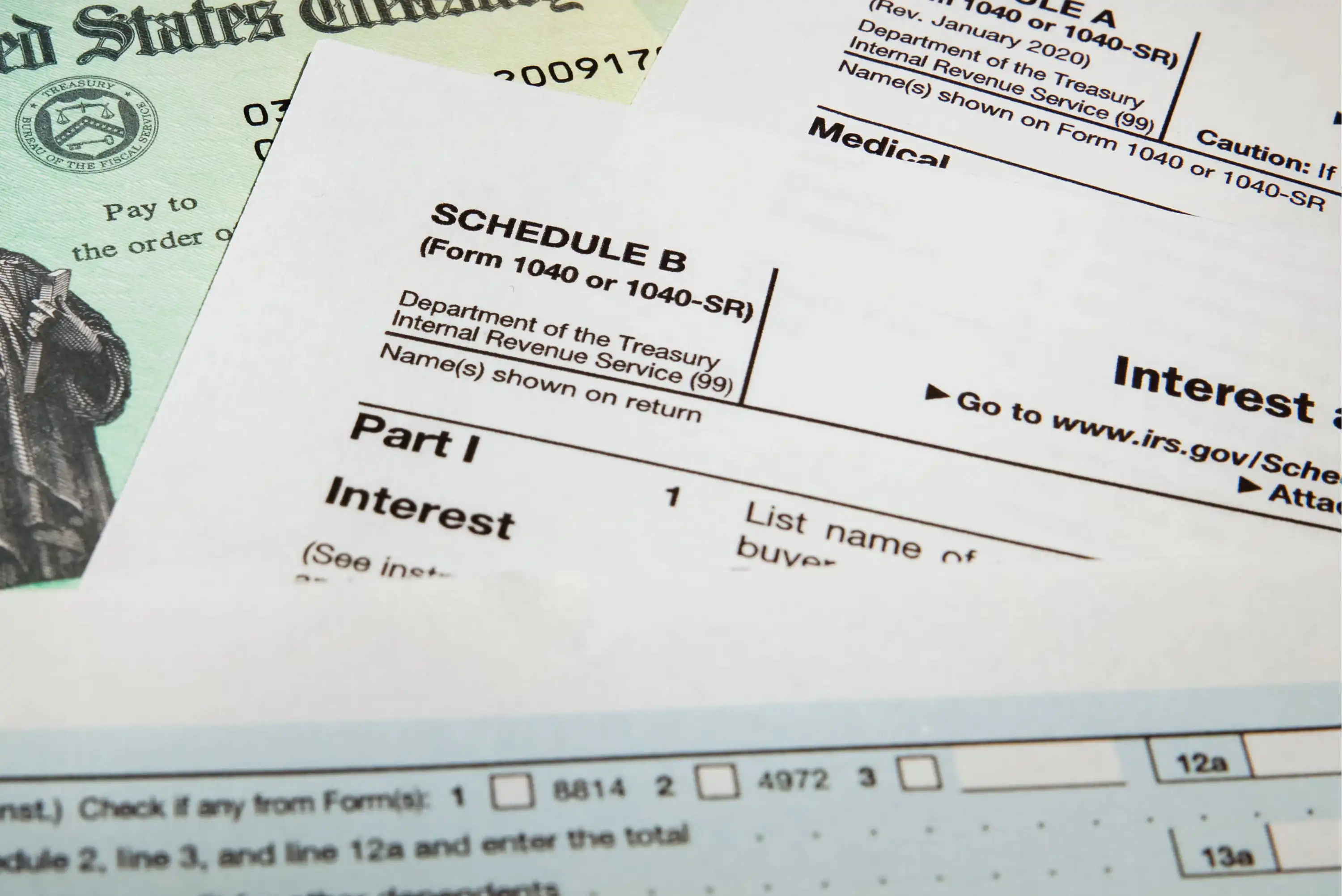 A close-up of U.S. tax documents, including a Schedule B form, a partial check, and a tax return form, highlighting text related to interest and income reporting.