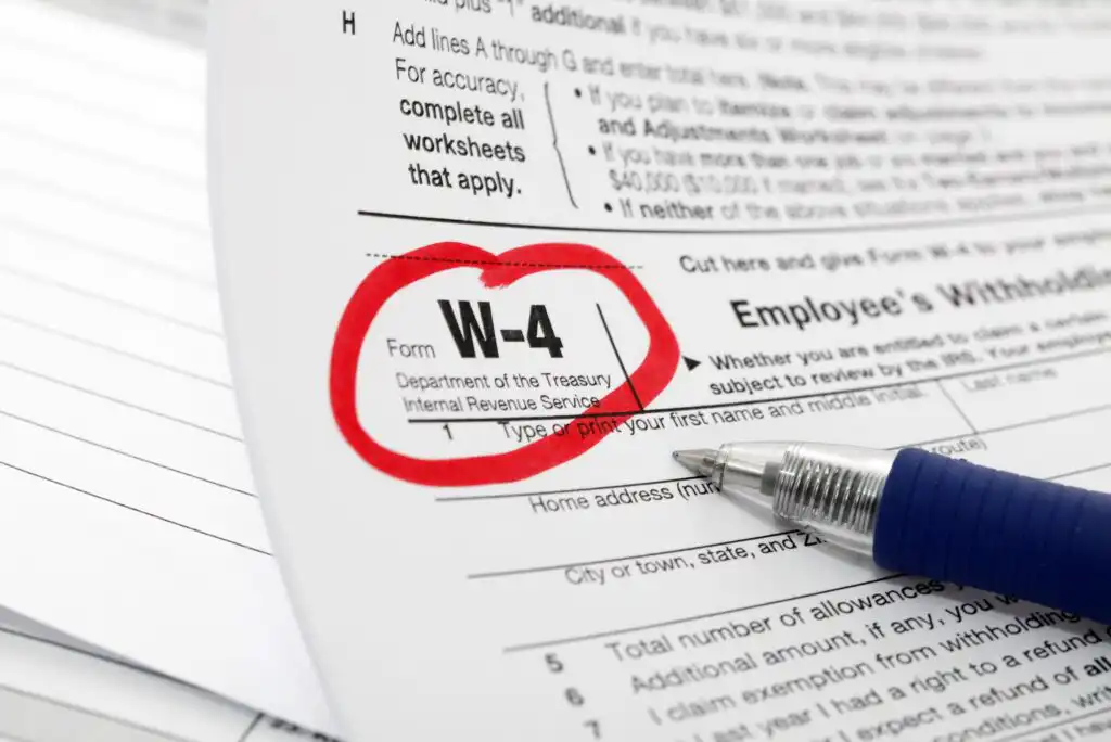 A close-up of a W-4 tax form with W-4 circled in red ink, partially covered by a blue pen, lying on top of other paperwork.