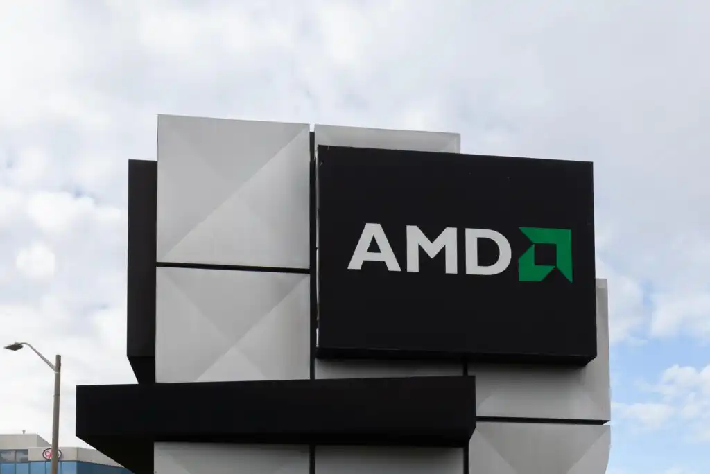 A building sign displays the AMD logo in white and green on a black background, with geometric gray tiles and a cloudy sky in the background.