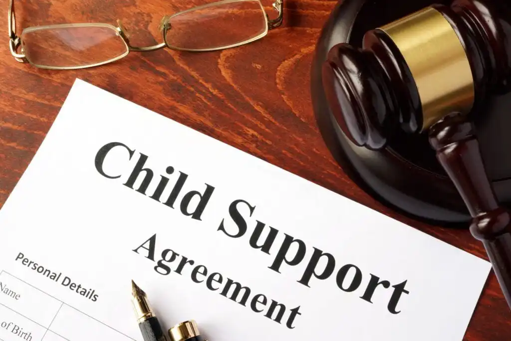 A Child Support Agreement document on a desk with a fountain pen, a judge’s gavel, and a pair of eyeglasses nearby.
