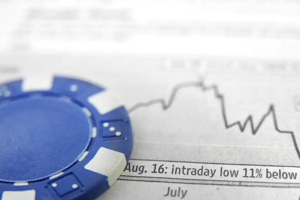 A blue casino chip lies on a financial newspaper showing a stock chart with a sharp downward trend and the words “Aug. 16: intraday low 11% below.”.