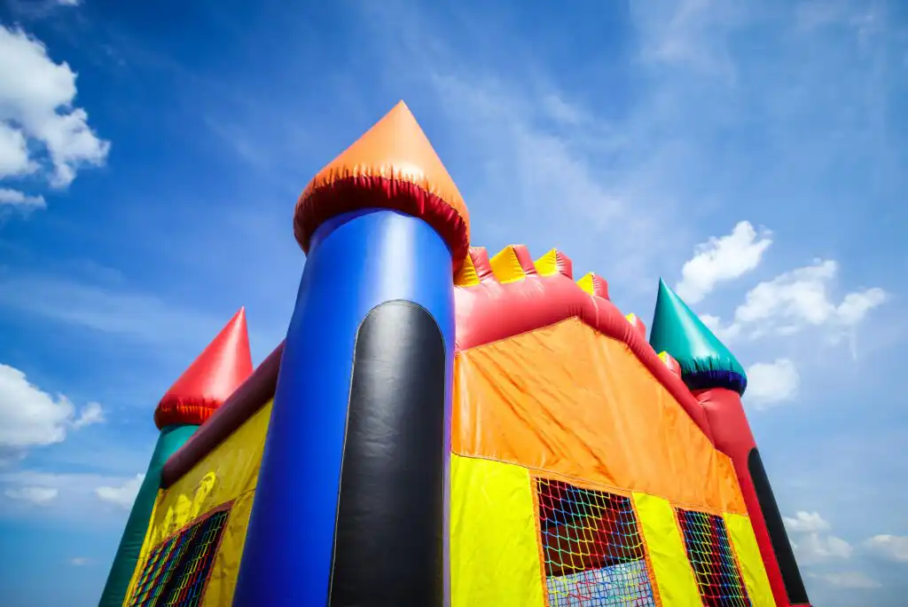 A colorful inflatable bounce house with pointed towers stands under a bright blue sky with scattered clouds, creating a playful and festive atmosphere.