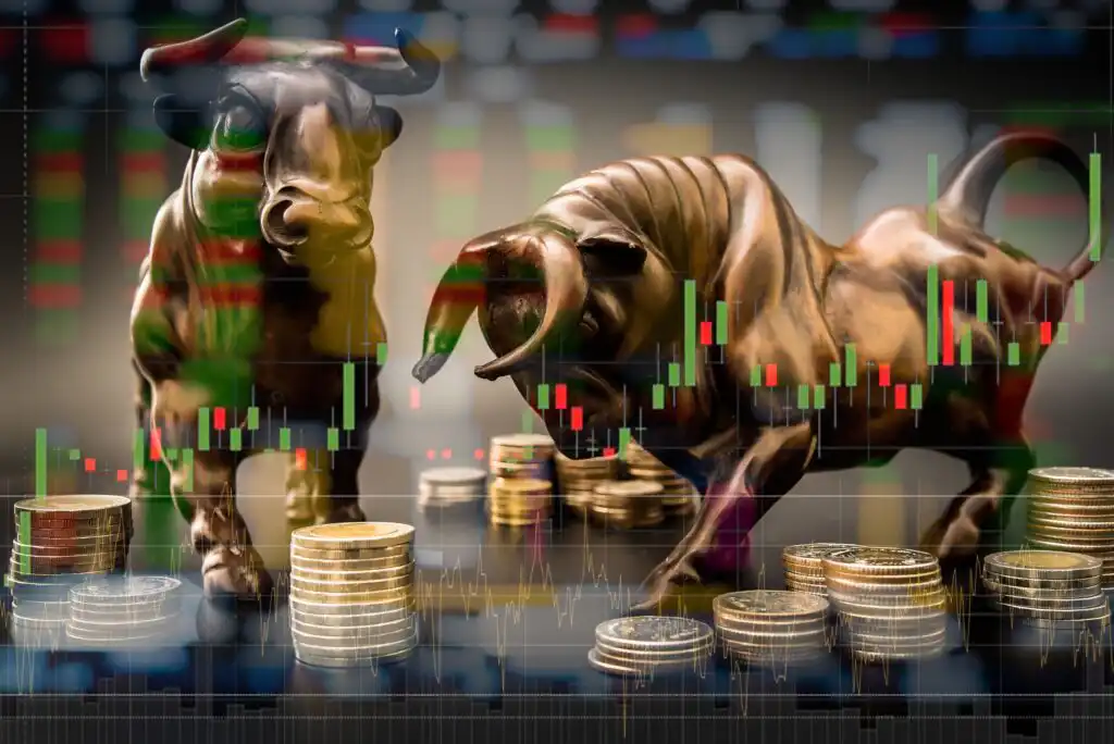 Bronze bull and bear figurines stand among stacks of coins, overlaid with colorful stock market graphs and candlestick charts, symbolizing financial markets and economic trading trends.