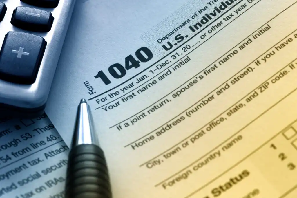 A close-up of a U.S. 1040 individual income tax form with a pen pointing toward it and part of a calculator visible on the left side, symbolizing tax preparation.