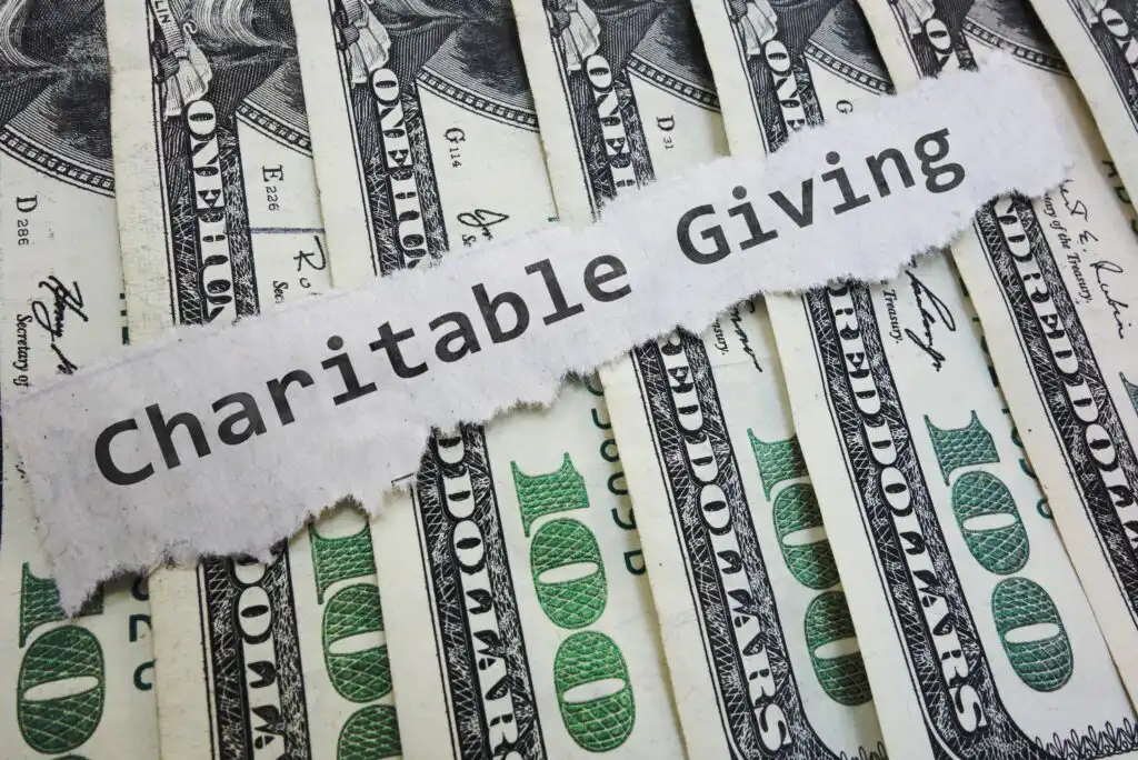 A torn piece of paper with the words Charitable Giving lies across several overlapping U.S. $100 bills.