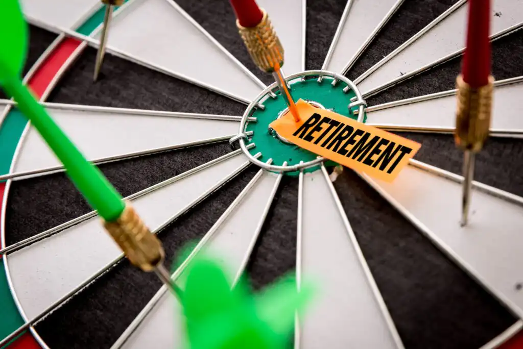 A close-up of a dartboard with several darts hitting the bullseye, where a yellow note labeled RETIREMENT is placed at the center.