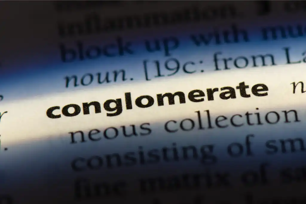 A close-up of a dictionary page with the word conglomerate in bold, surrounded by its definition, under a beam of light highlighting the word.