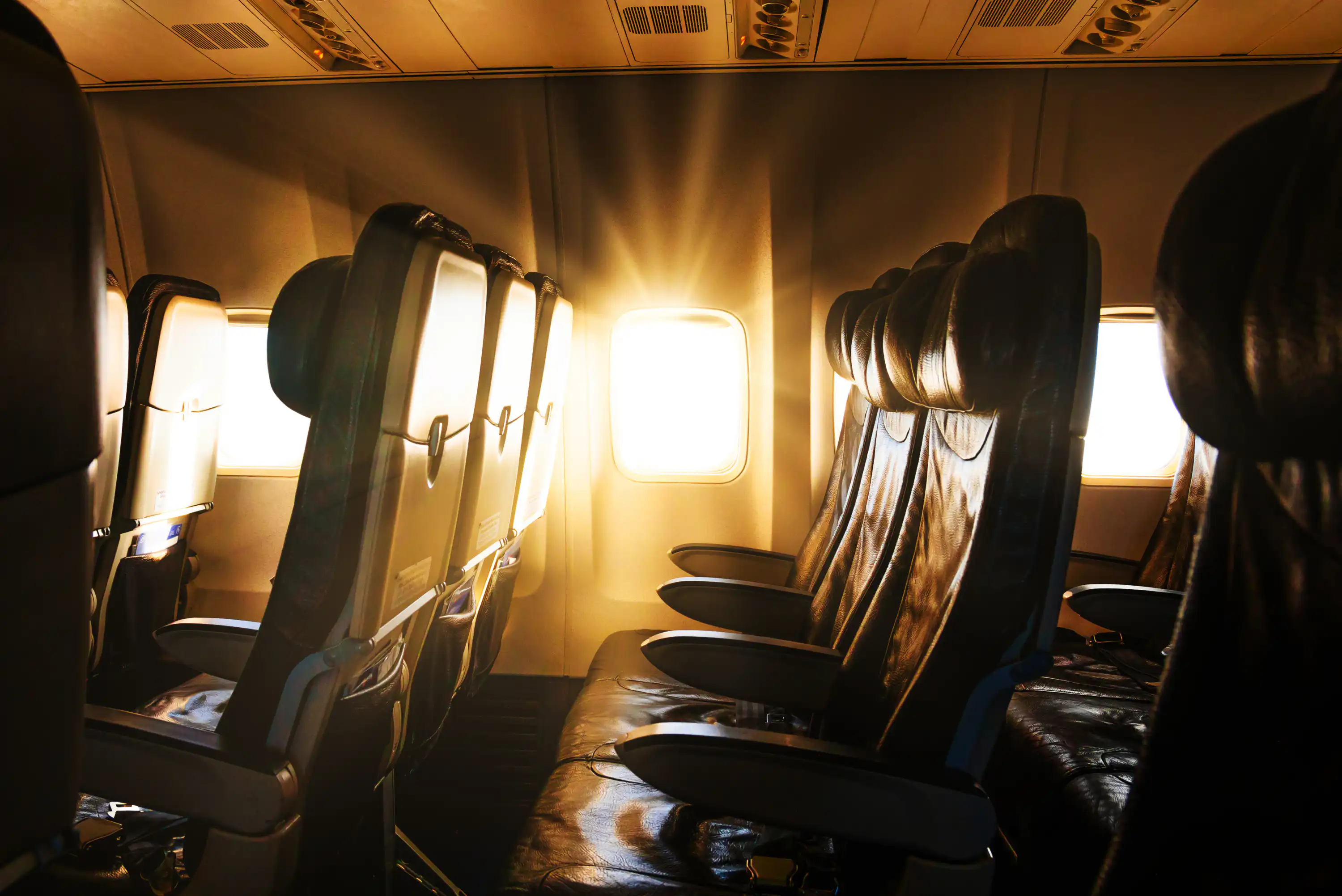 Empty airplane seats bathed in warm sunlight streaming through a window, creating a bright glow inside the cabin.