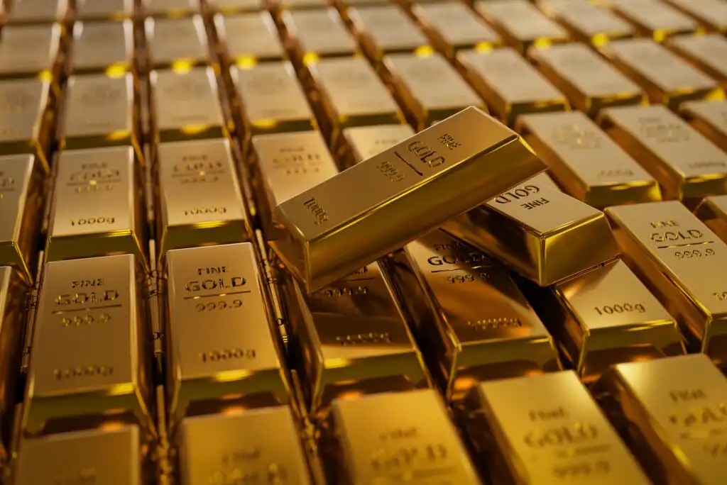 Rows of shiny gold bars are stacked closely together, with a few bars placed diagonally on top. Each gold bar is labeled “FINE GOLD 999.9” and “1000g.” The scene reflects wealth and luxury.