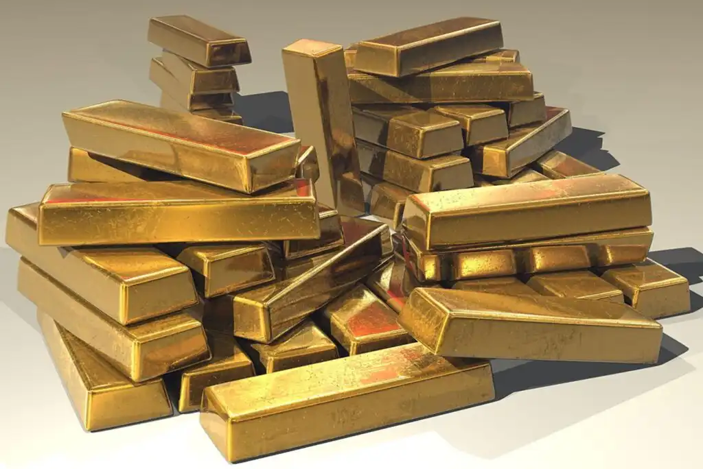 A large pile of shiny gold bars stacked unevenly on a plain surface, reflecting light and showing slight surface imperfections.