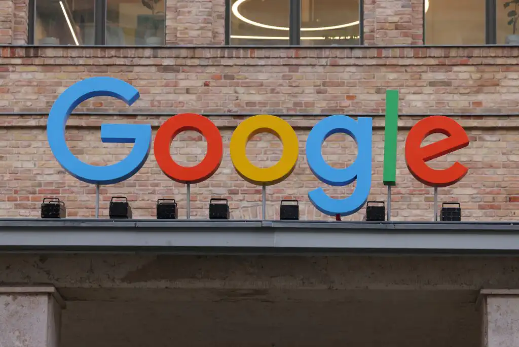 The colorful Google logo is displayed on the exterior of a brick building, with large, bold letters in blue, red, yellow, and green.