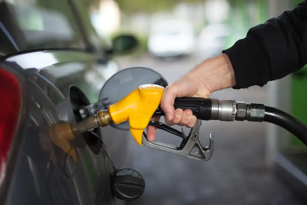 A person’s hand holding a yellow fuel pump nozzle, refueling a car at a gas station.