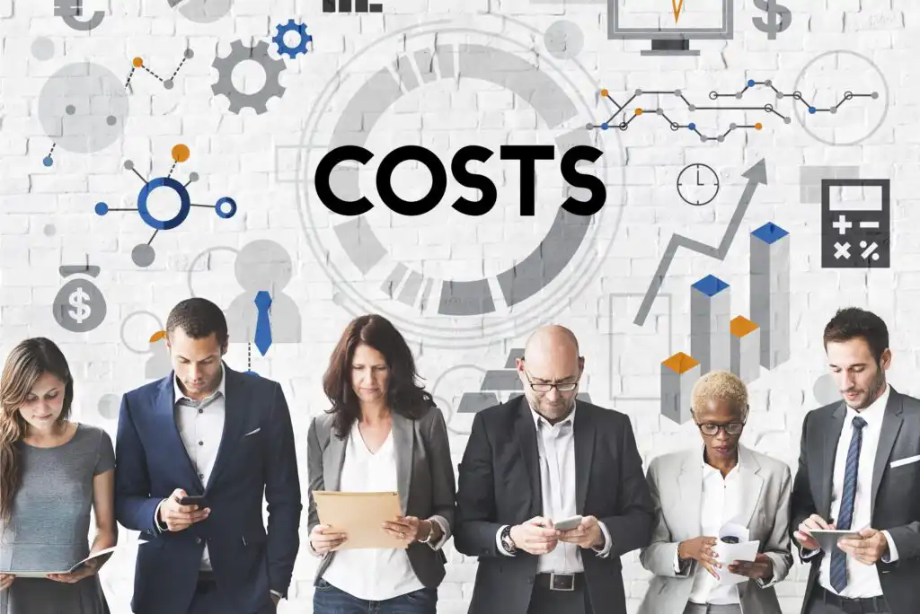 Six business professionals stand in a row using electronic devices, with the word COSTS and various business-related icons and graphs displayed on a white brick wall behind them.