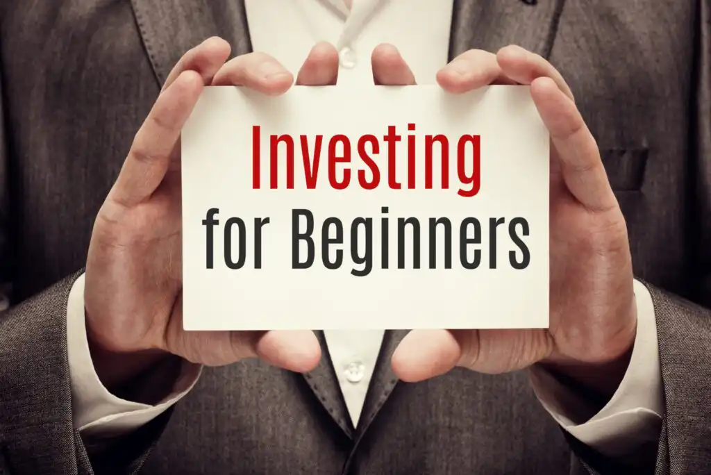 Close-up of a person in a suit holding a card that reads Investing for Beginners in bold red and gray letters.