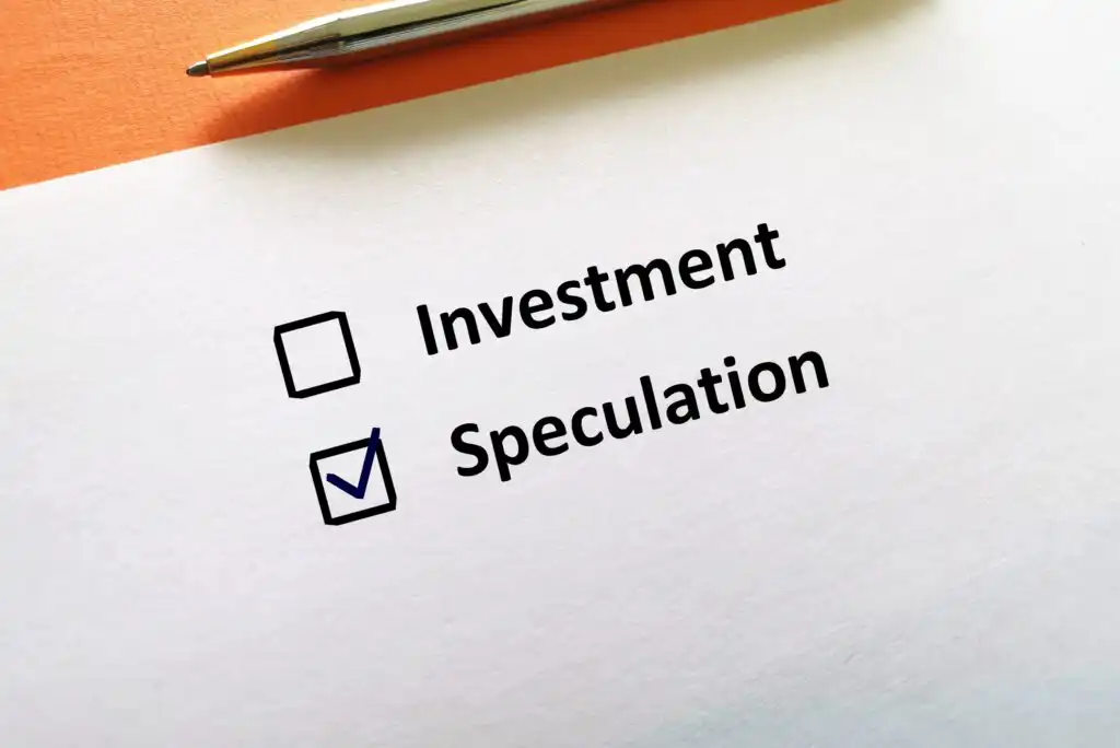 A paper with two checkboxes labeled Investment and Speculation. The Speculation box is checked with a blue mark, and a pen lies above the text.